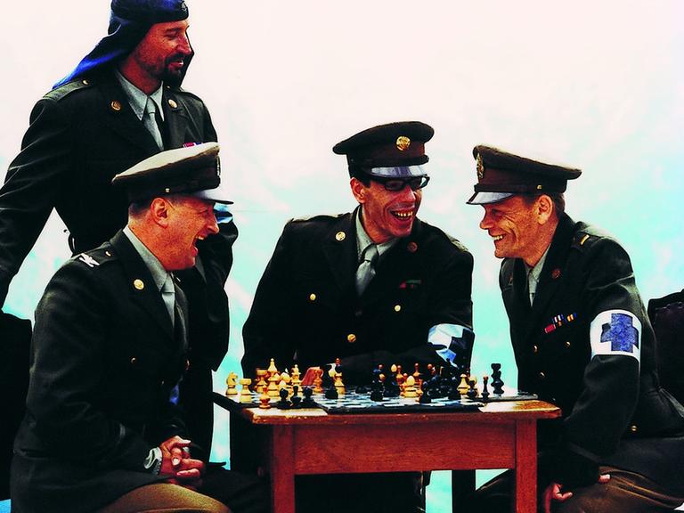 Die Musiker der Band Laibach sitzen in Uniformen um einen Tisch mit Schachspiel zusammen.