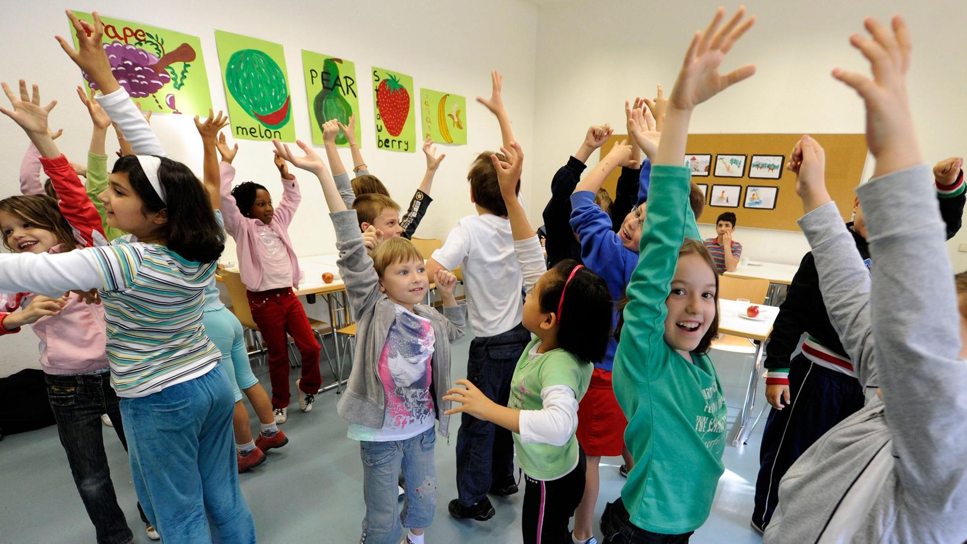 Kinder stehen in einem Klassenraum und heben ihre Arme, an den Wänden bunte Bilder. Kinder stehen in einem Klassenraum und heben ihre Arme, an den Wänden bunte Bilder.