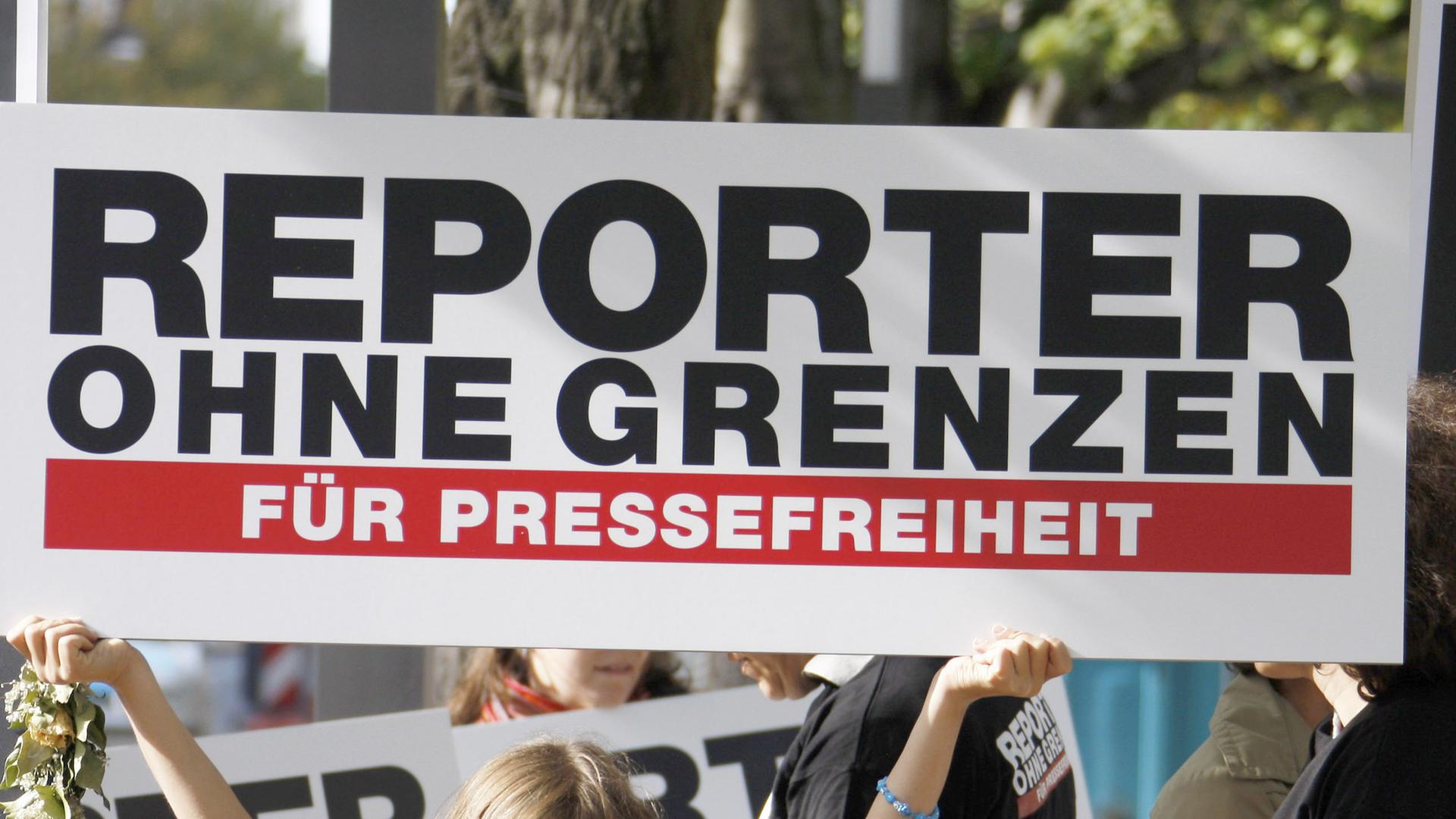 Dein Schild mit der Aufschrift "Reporter ohne Grenzen - Für Pressefreiheit" wird hochgehalten.