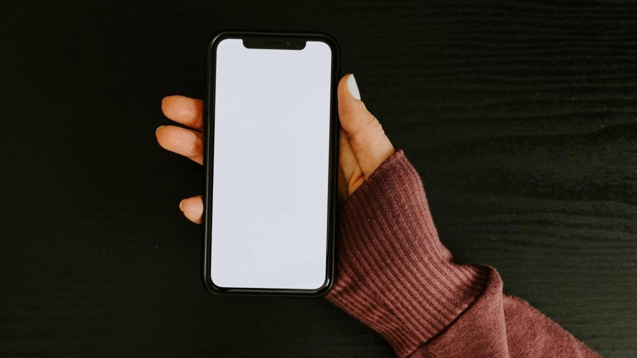 Auf dem Bild ist eine Hand zu sehen, die ein iPhone hält. Auf dem Bild ist eine Hand zu sehen, die ein iPhone hält.