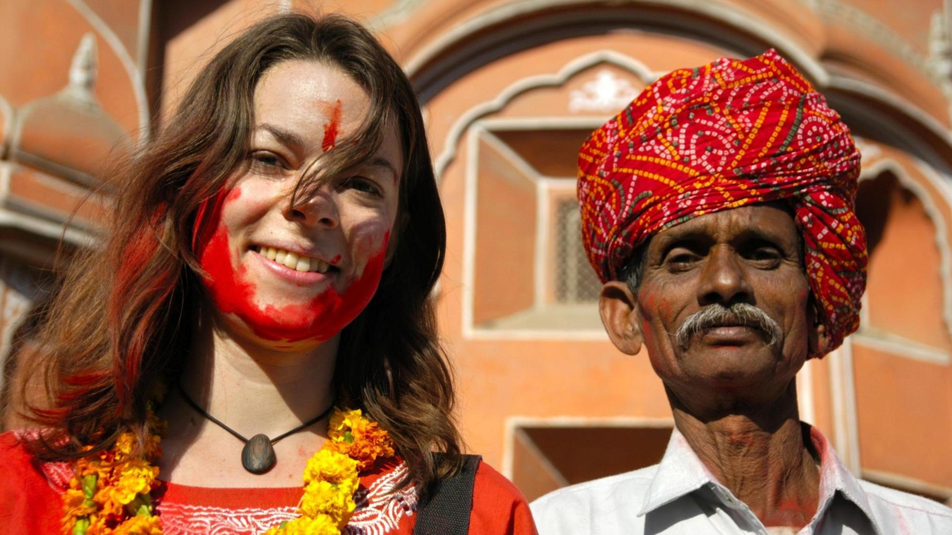 Junge Touristin mit roter Farbe im Gesicht neben einem Rajputen mit rotem Turban vor dem Palast der Winde in Jaipur in Indien. Junge Touristin mit roter Farbe im Gesicht neben einem Rajputen mit rotem Turban vor dem Palast der Winde in Jaipur in Indien.
