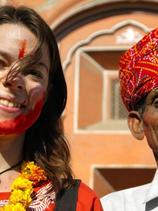 Junge Touristin mit roter Farbe im Gesicht neben einem Rajputen mit rotem Turban vor dem Palast der Winde in Jaipur in Indien.