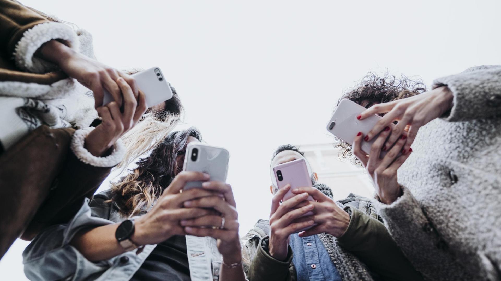 Vier junge Menschen stehen in einem Halbkreis mit ihren Smartphones.