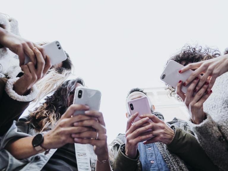 Vier junge Menschen stehen in einem Halbkreis mit ihren Smartphones.
