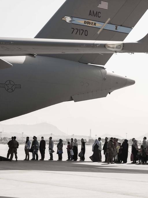 Auf dem Flugfeld des Flughafens Kabul stehen Menschen vor einem Evakuierungsflugzeug Schlange.