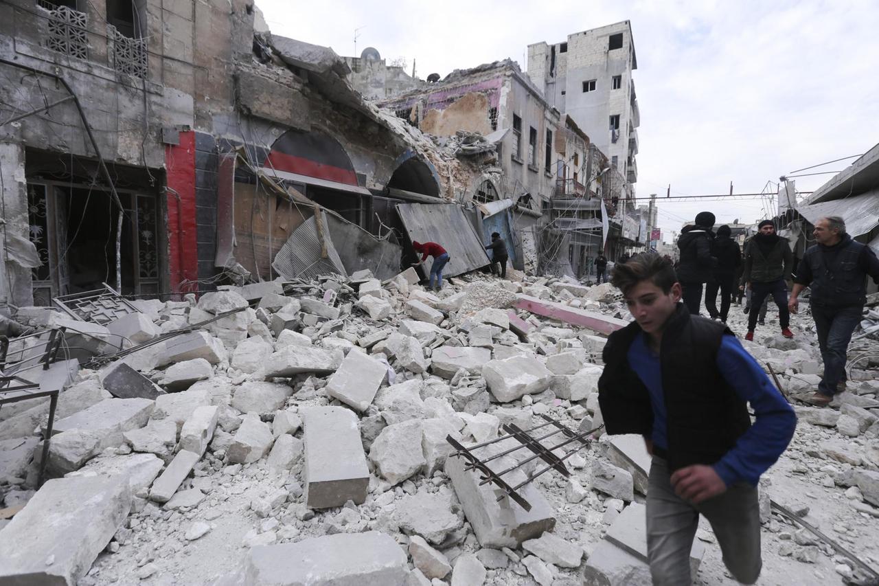 Menschen laufen durch Trümmer einer durch Kämpfe und Luftangriffen zerstörten Häuserzeile.