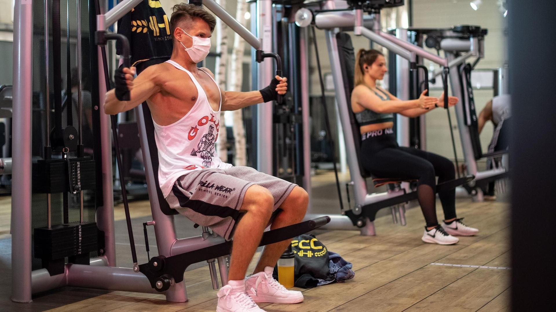 Ein Mann mit Mund-Schutz trainiert an einem Gerät im Fitness-Studio. Ein Mann mit Mund-Schutz trainiert an einem Gerät im Fitness-Studio.