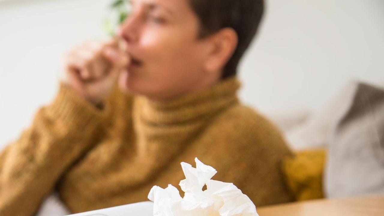 Eine kranke Frau hustet, vor ihr auf einem Tisch liegt ein zusammen geknülltes Taschen-Tuch. Eine kranke Frau hustet, vor ihr auf einem Tisch liegt ein zusammen geknülltes Taschen-Tuch.