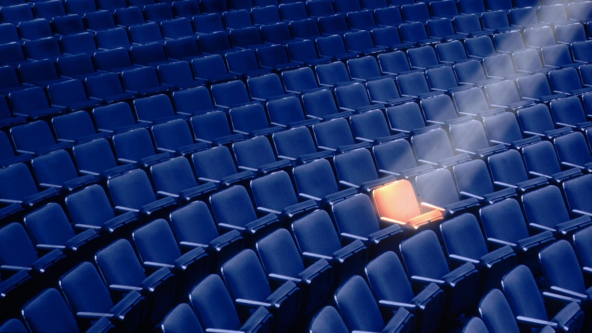 Ein leerer Theatersaal mit einem Spotlight auf einen einzelnen Sitz. Ein leerer Theatersaal mit einem Spotlight auf einen einzelnen Sitz.