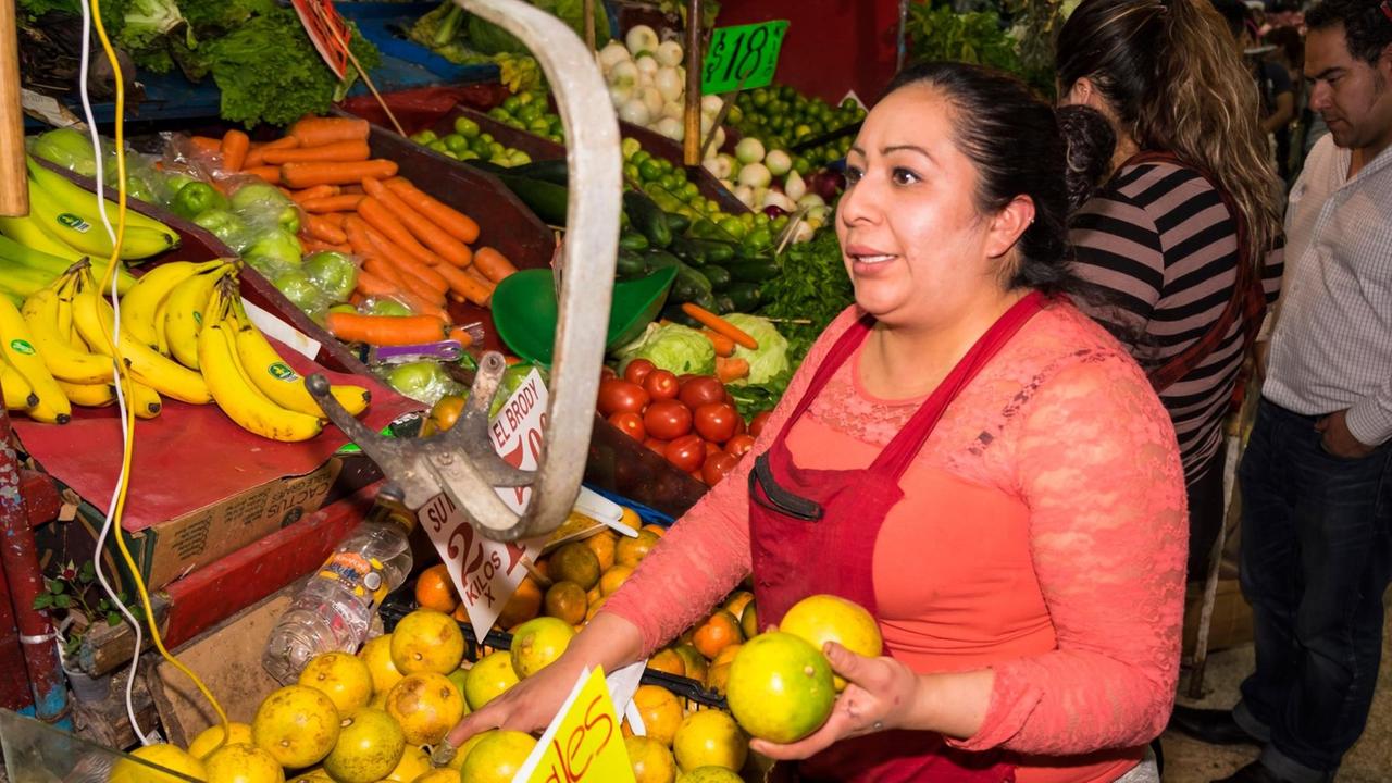 Yasmin Sierra an ihrem Obststand auf dem Markt in Santa María de Ribera in Mexiko-Stadt. Ihre Kinder werden bei Yolia betreut, da sie sich wegen der Arbeit nicht um sie kümmern kann.