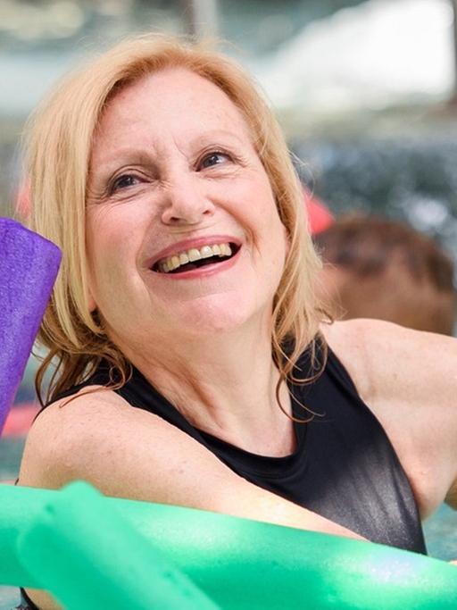 Das Bild zeigt die Schauspielerin Maren Kroymann, die im Schwimmbecken mit einer Schwimmnudel schwimmt.