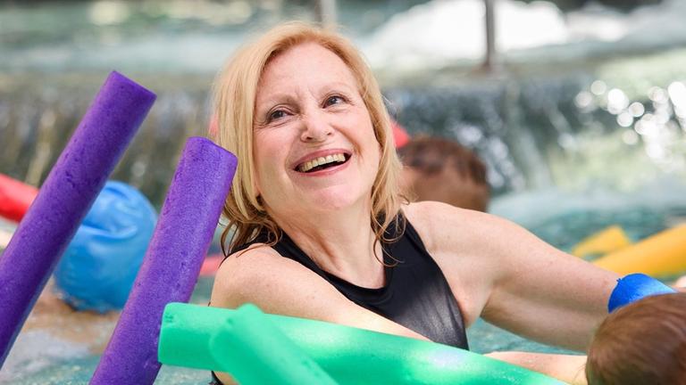 Das Bild zeigt die Schauspielerin Maren Kroymann, die im Schwimmbecken mit einer Schwimmnudel schwimmt. Das Bild zeigt die Schauspielerin Maren Kroymann, die im Schwimmbecken mit einer Schwimmnudel schwimmt.