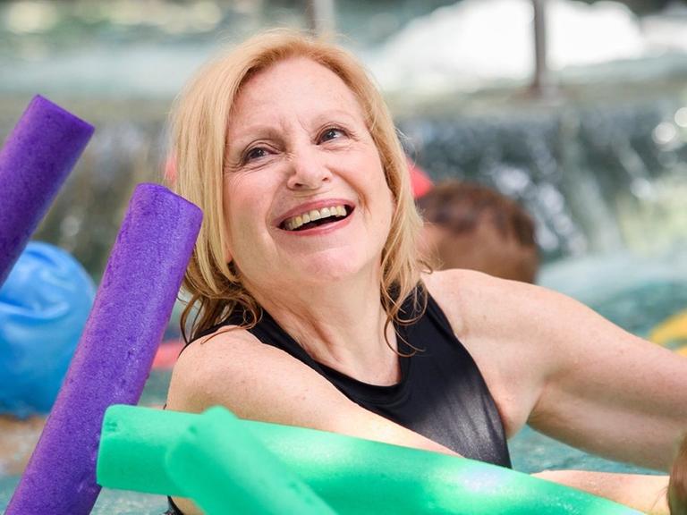 Das Bild zeigt die Schauspielerin Maren Kroymann, die im Schwimmbecken mit einer Schwimmnudel schwimmt.