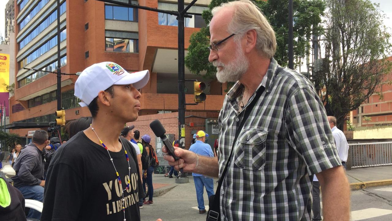 Burkhard Birke unterhält sich mit Mikrofon in der Hand mit einen Demonstranten in Caracas, Venezuela. Burkhard Birke unterhält sich mit Mikrofon in der Hand mit einen Demonstranten in Caracas, Venezuela.