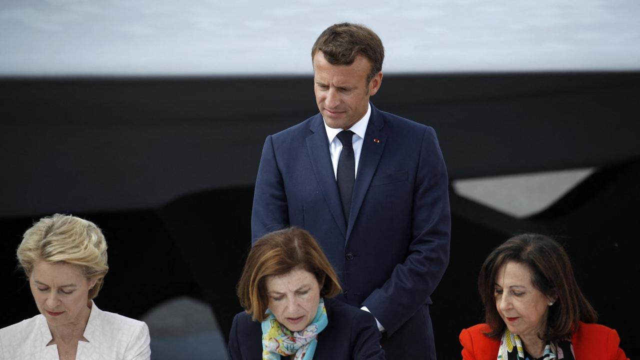 Frankreichs Präsident Emmanuel Macron (stehend) im Juni 2019 mit den damaligen Verteidigungsministerinnen Ursula von der Leyen, Florence Parly und Margarita Robles (von links nach rechts)  bei der Unterzeichnung eines Abkommens zum Future Combat Air System (FCAS) am Flughafen Le Bourget bei Paris