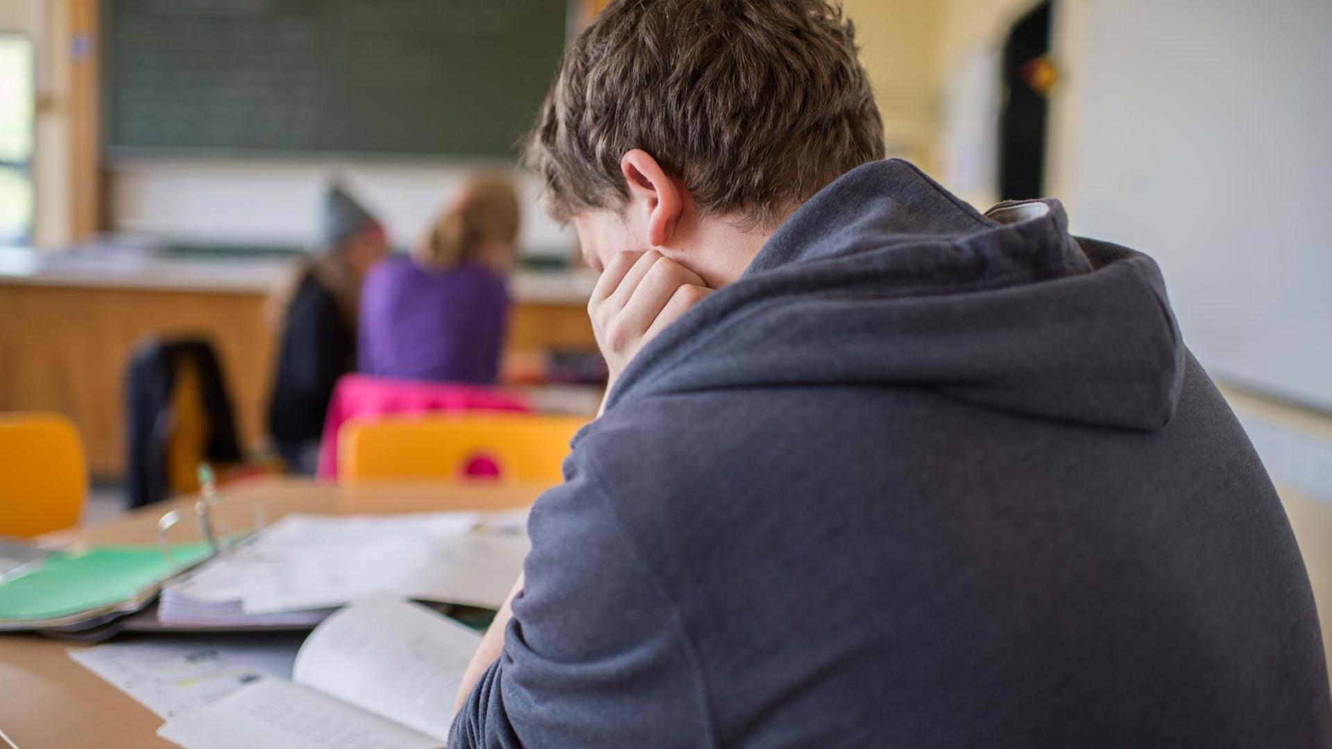 Ein Schüler sitzt im Unterricht an einem Schreibtisch und stützt seinen Kopf Ein Schüler sitzt im Unterricht an einem Schreibtisch und stützt seinen Kopf
