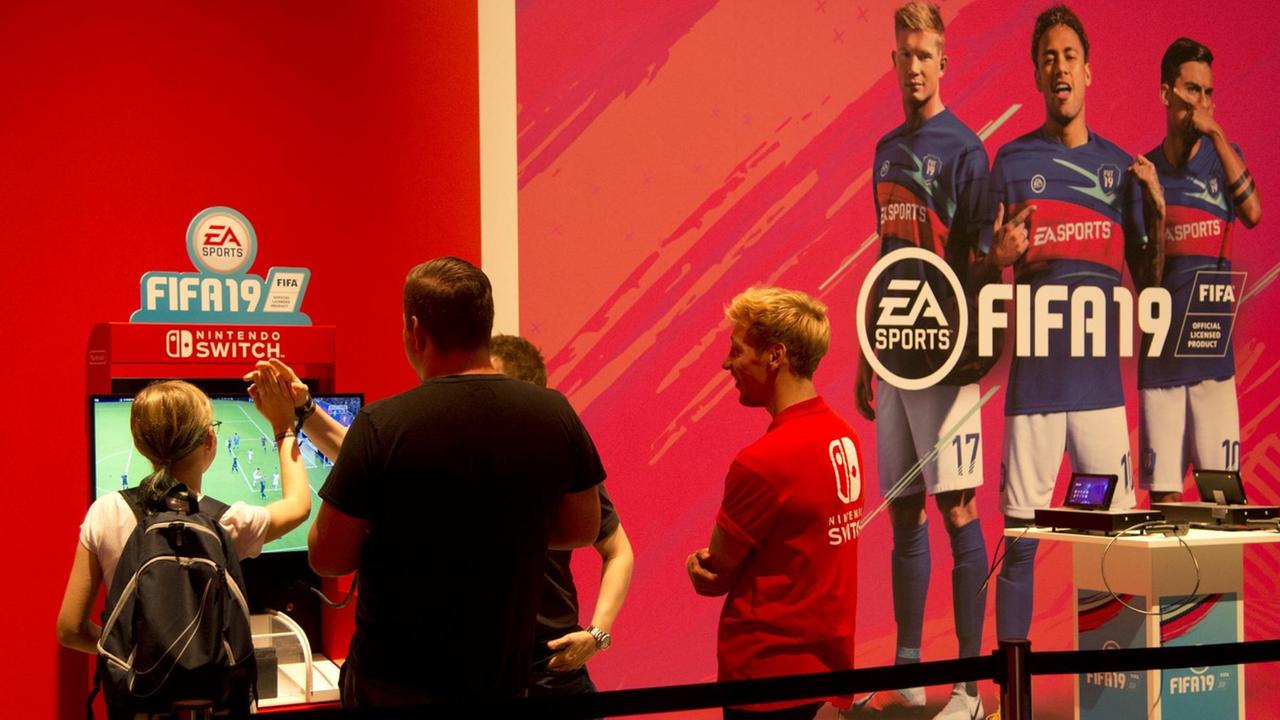 Messe-Besucher spielen das Spiel FIFA19 am Bildschirm Messe-Besucher spielen das Spiel FIFA19 am Bildschirm