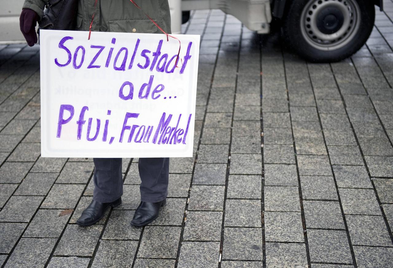 Eine Demonstrantin mit einem Schild auf dem Steht: "Sozialstaat ade Pfui Frau Merkel" Symbolfoto,  