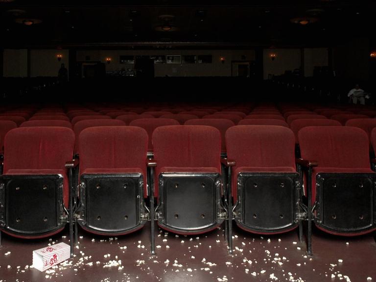 Ein leerer Kinosaal mit samtroten Sesseln, verstreutes Popcorn liegt vor der ersten Reihe auf dem Boden.