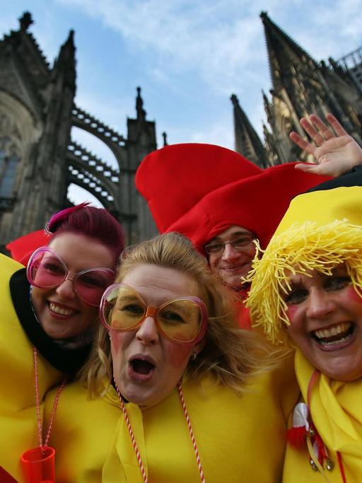 Vier Karnevalisten in Hühnerkostümen posieren vor dem Kölner Dom für die Kamera.