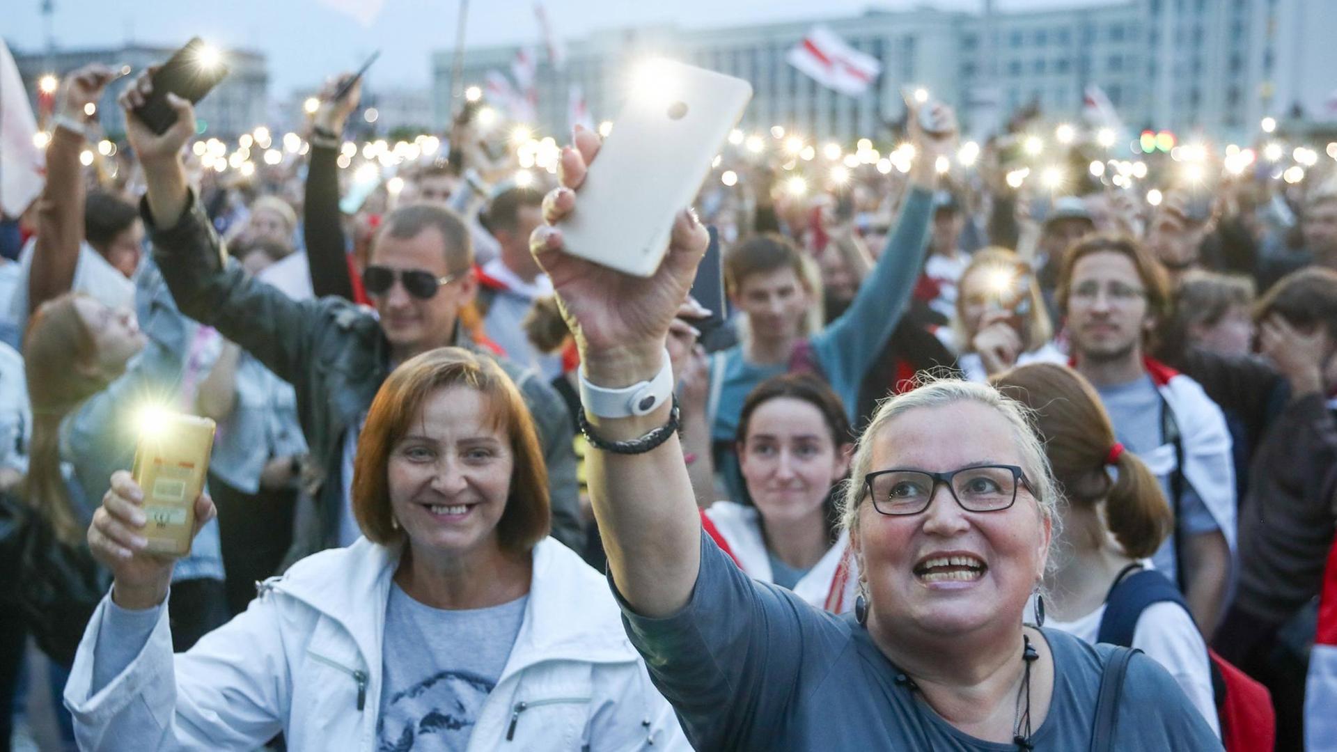 Protestierende Menschen halten auf dem Unabhängigkeitsplatz in Minsk ihre Smartphones mit Blitzlicht in die Höhe.