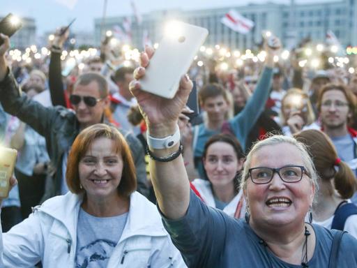 Protestierende Menschen halten auf dem Unabhängigkeitsplatz in Minsk ihre Smartphones mit Blitzlicht in die Höhe.