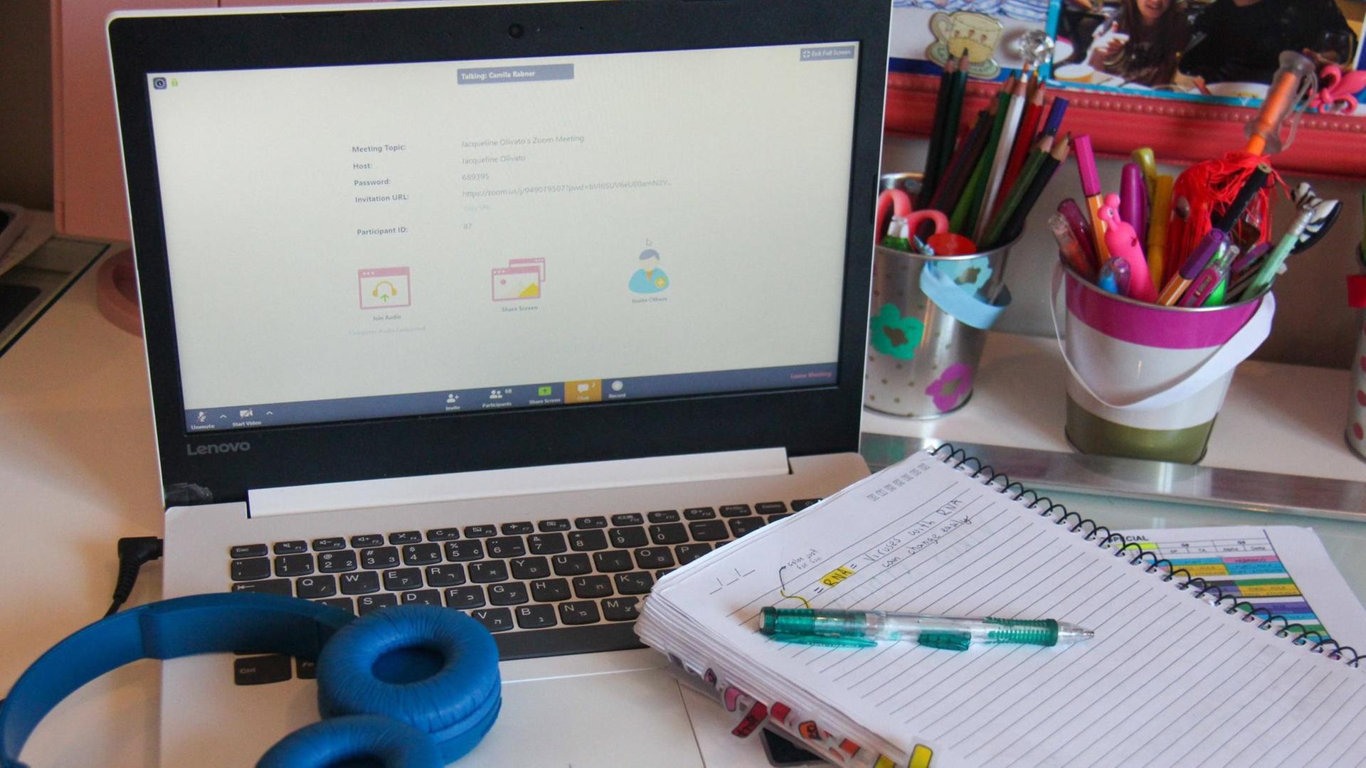 Ein Laptop, ein Notizblock und Kopfhörer eines Schulkinds liegen auf einem Schreibtisch