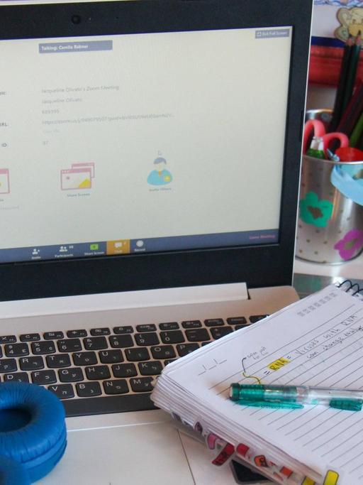 Ein Laptop, ein Notizblock und Kopfhörer eines Schulkinds liegen auf einem Schreibtisch