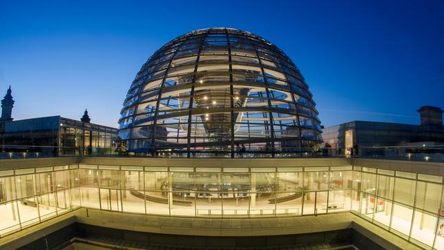 Im Abendlicht gehen in Berlin Besucher an der Kuppel des Reichstags entlang.