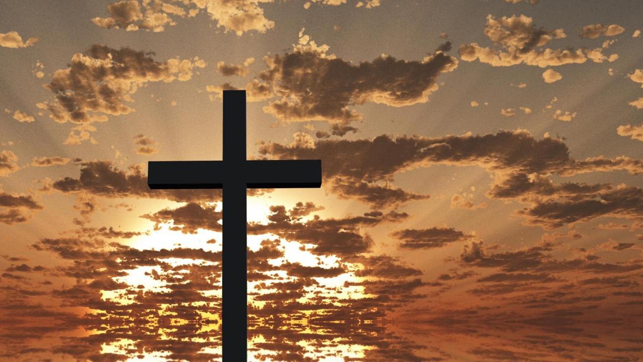 Ein großes Kreuz ragt dem rot glühendem Himmel voller Wolken bei einem Sonnenaufgang entgegen. Ein großes Kreuz ragt dem rot glühendem Himmel voller Wolken bei einem Sonnenaufgang entgegen.