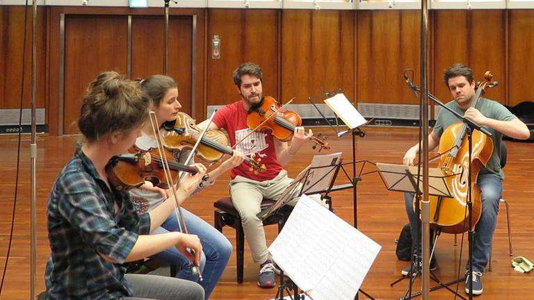 Die vier Musiker des Aris Quartett sitzen mit ihren Instrumenten im Kreis um ihre Notenpulte im Deutschlandfunk Kammermusiksaal. Die vier Musiker des Aris Quartett sitzen mit ihren Instrumenten im Kreis um ihre Notenpulte im Deutschlandfunk Kammermusiksaal.