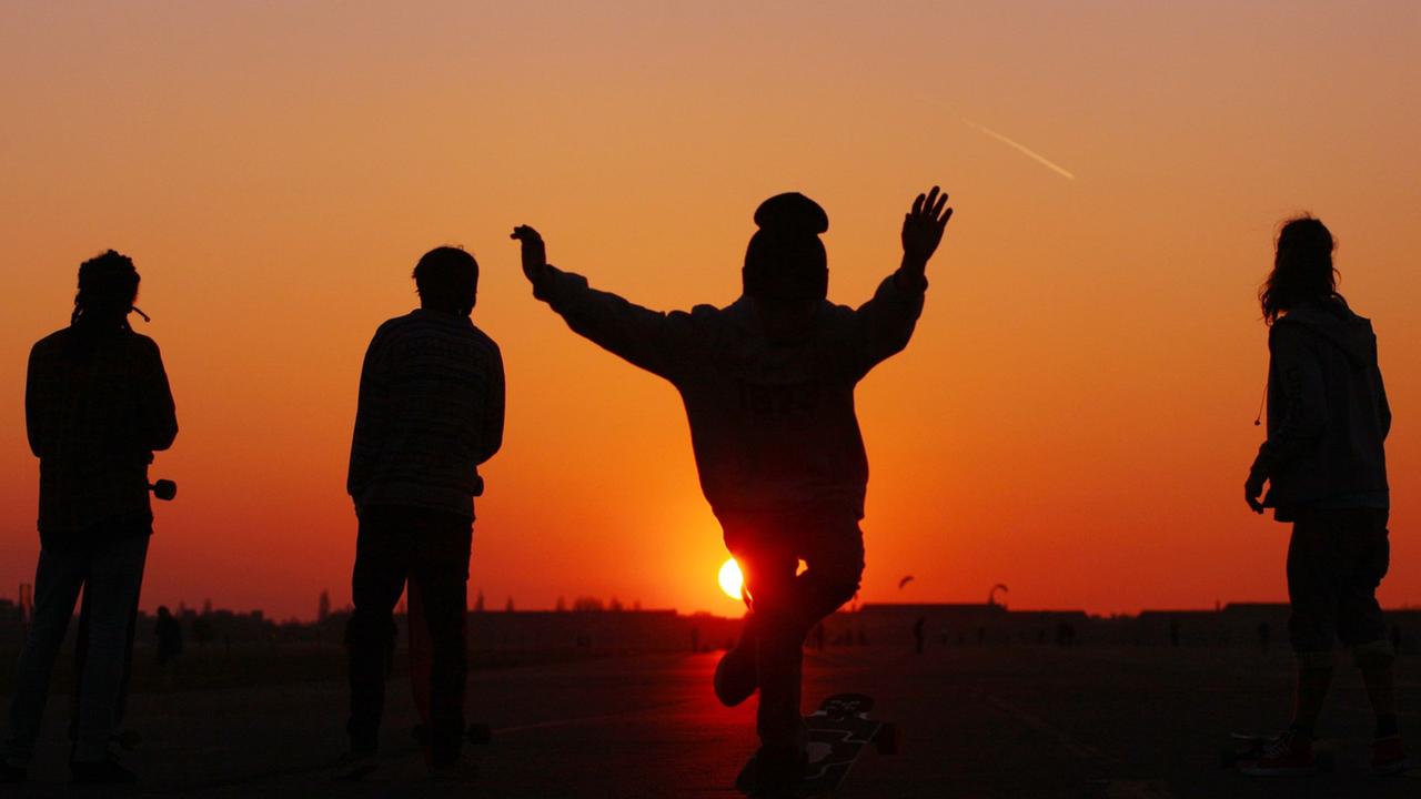 Skateboarder, darunter auch ein Junge (2.v.r.), fahren im Abendlicht auf dem Tempelhofer Feld, dem größten Park Berlins, auf dem Gelände des ehemaligen Flughafens Tempelhof, in Berlin Skateboarder, darunter auch ein Junge (2.v.r.), fahren im Abendlicht auf dem Tempelhofer Feld, dem größten Park Berlins, auf dem Gelände des ehemaligen Flughafens Tempelhof, in Berlin
