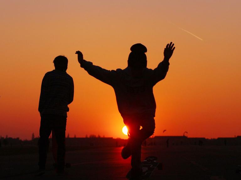 Skateboarder, darunter auch ein Junge (2.v.r.), fahren im Abendlicht auf dem Tempelhofer Feld, dem größten Park Berlins, auf dem Gelände des ehemaligen Flughafens Tempelhof, in Berlin