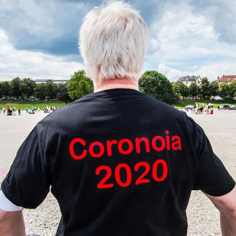 Man sieht einen Mann von hinten, der ein schwarzes T-Shirt mit dem roten Aufdruck "Coronoia 2020" trägt