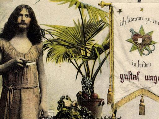 Der Wanderprediger Gustaf Nagel in einer Aufnahme um 1935 neben einem Banner auf dem steht: "ich komme zu euch in friden, gustaf nagel."