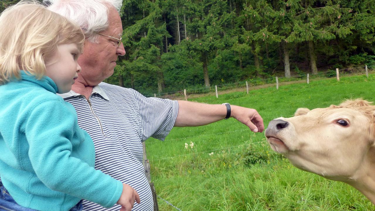 Günter, der Vater des Autors Thilo Schmidt, mit seiner Enkelin Pauline auf dem Arm, er streichelt eine Kuh