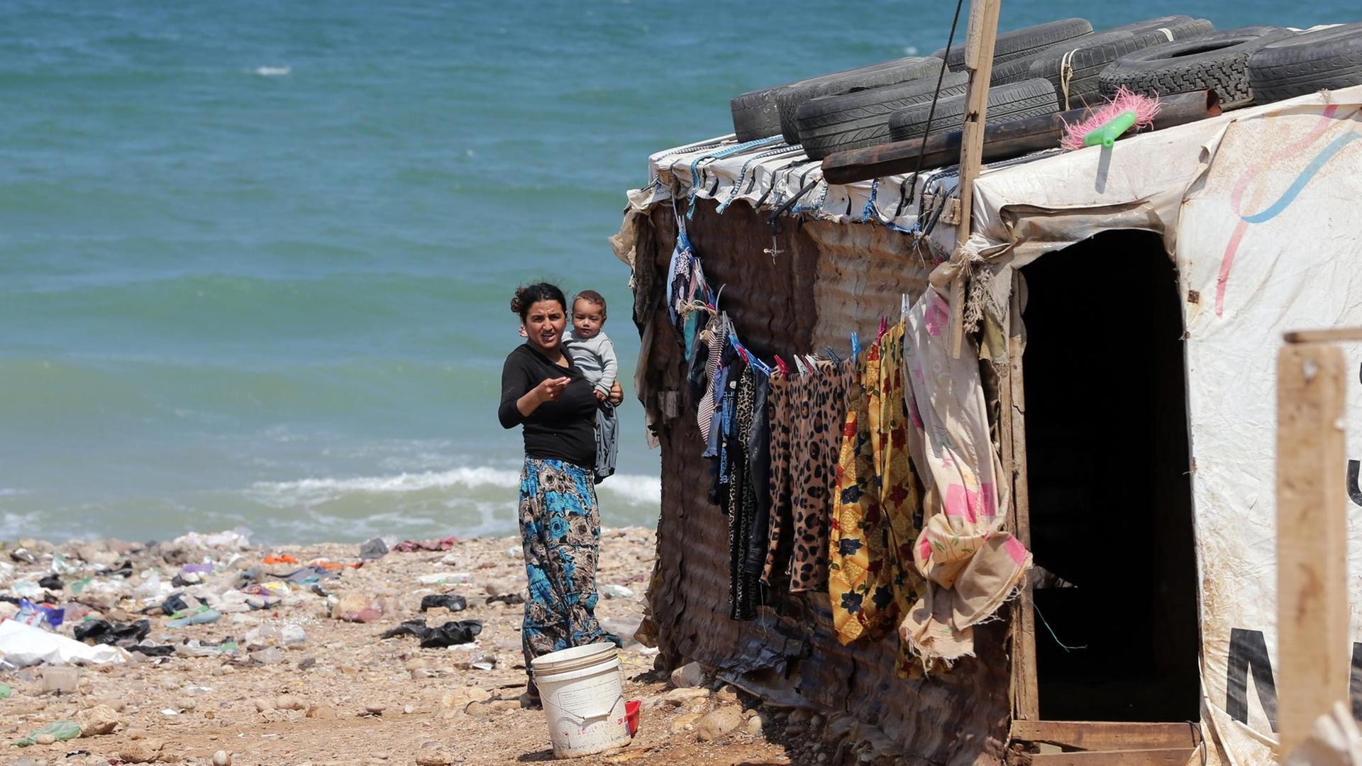 Eine Frau mit Kind hängt in einem illegalen Flüchtlingslager bei Beirut Wäsche auf.