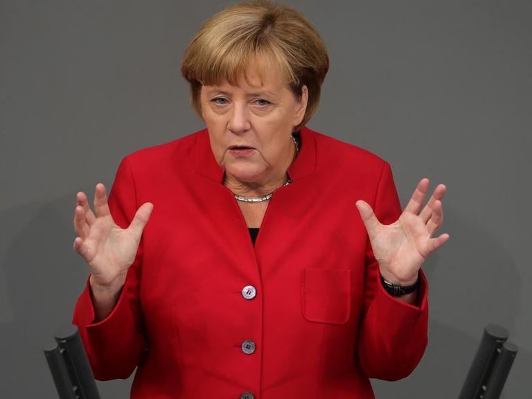 Merkel im roten Kostüm spricht und gestikuliert mit beiden Händen am Rednerpult.