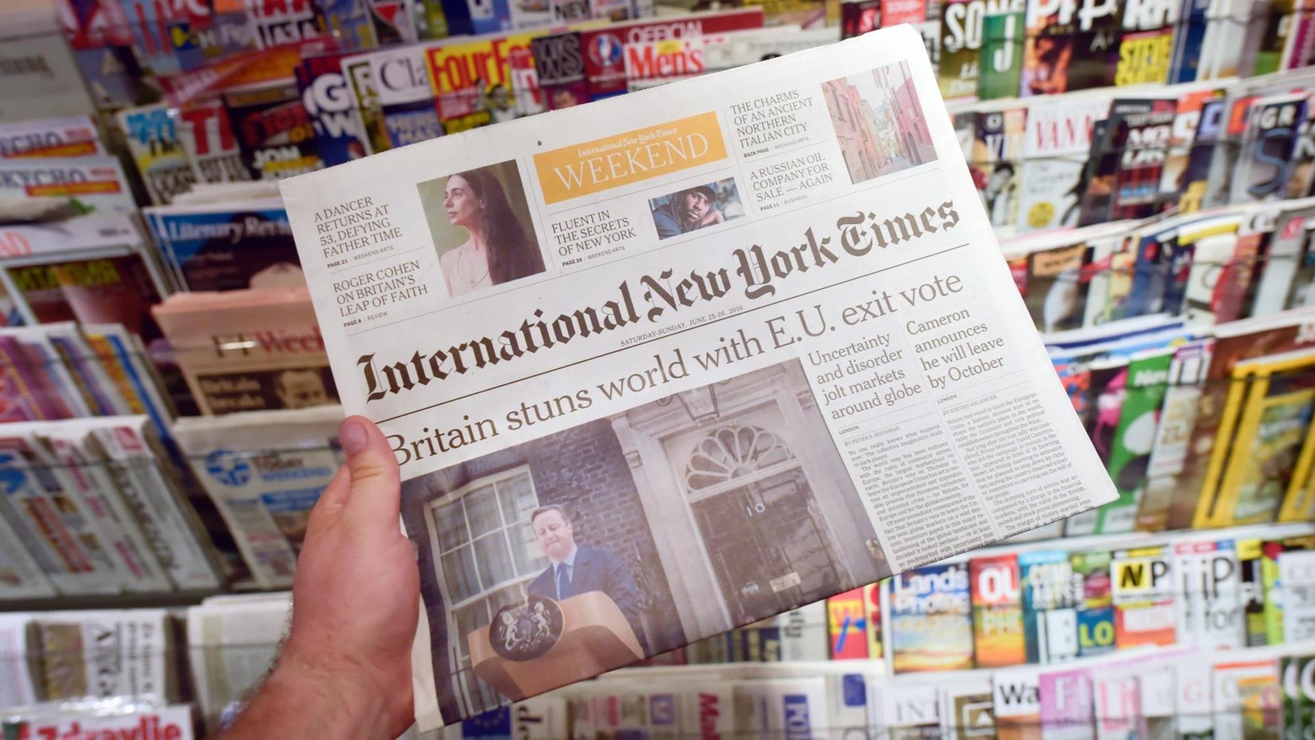 Eine Hand hält die International New York Times in Berlin in einem Kiosk.