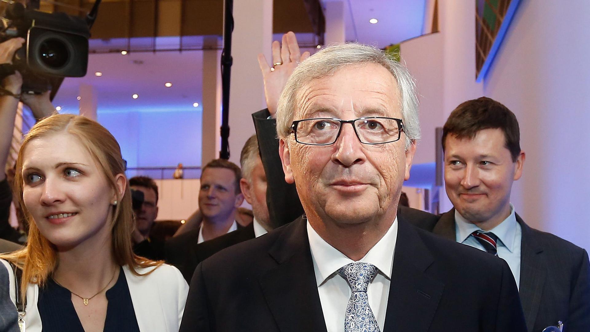 Jean-Claude Juncker am Abend der Europawahl in Brüssel. Hinter ihm stehen eine Frau und ein winkender Mann. Jean-Claude Juncker am Abend der Europawahl in Brüssel. Hinter ihm stehen eine Frau und ein winkender Mann.
