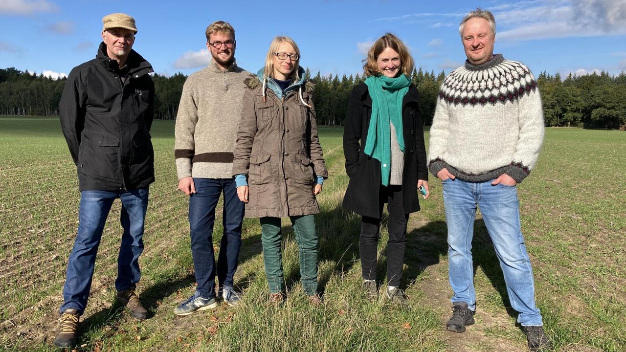 Fünf Menschen stehen auf einem Feld in der Sonne und schauen lächelnd in die Kamera. Fünf Menschen stehen auf einem Feld in der Sonne und schauen lächelnd in die Kamera.