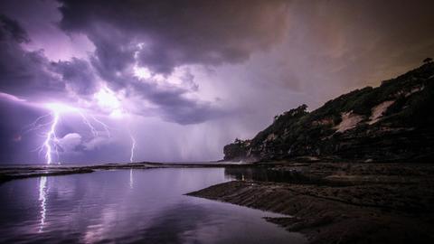 Ein Blitz schlägt ein über dem Meer an einer Küste.
