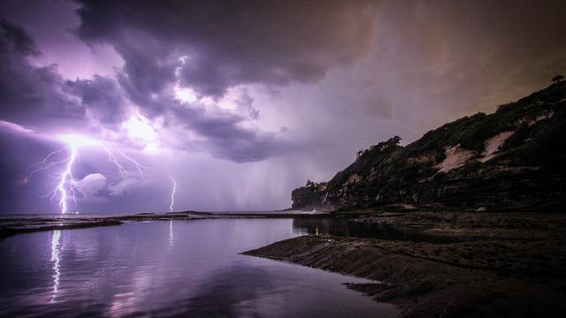 Ein Blitz schlägt ein über dem Meer an einer Küste.
