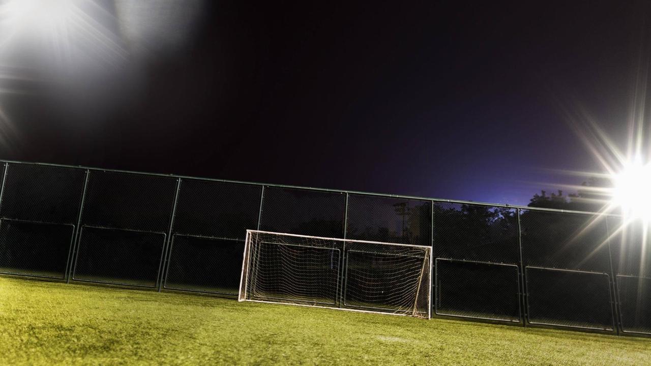 Ein Fußballfeld wird in der Dunkelheit von Flutlicht ausgeleuchtet.