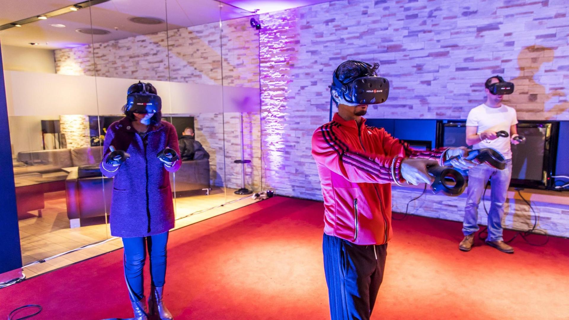 Mithilfe von VR-Brillen können Spieler gemeinsam in virtuelle Spielwelten eintauchen. Zu sehen sind Spieler im HoloCafe Düsseldorf, einer Art Spielhalle für Virtual Reality Spiele, in dem bis zu 4 Spieler mit- oder gegeneinander spielen können. Mithilfe von VR-Brillen können Spieler gemeinsam in virtuelle Spielwelten eintauchen. Zu sehen sind Spieler im HoloCafe Düsseldorf, einer Art Spielhalle für Virtual Reality Spiele, in dem bis zu 4 Spieler mit- oder gegeneinander spielen können.