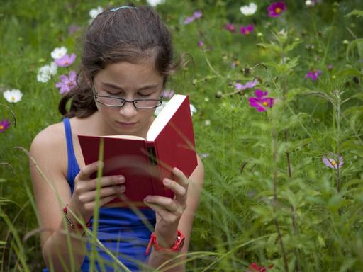 Ein elfjähriges Mädchen sitzt lesend auf einer Blumenwiese.
