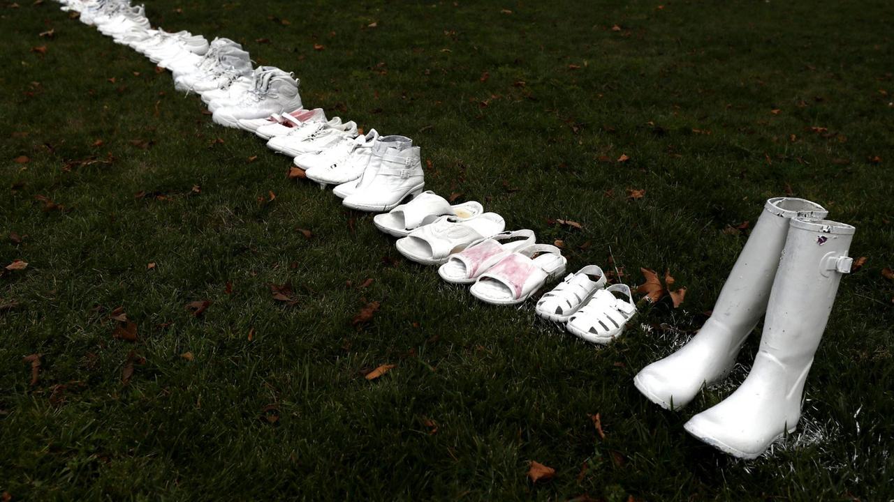 Eine Reihe weiß angesprühter Paar Schuhe zieht sich von oben links nach unten rechts durch das Bild.