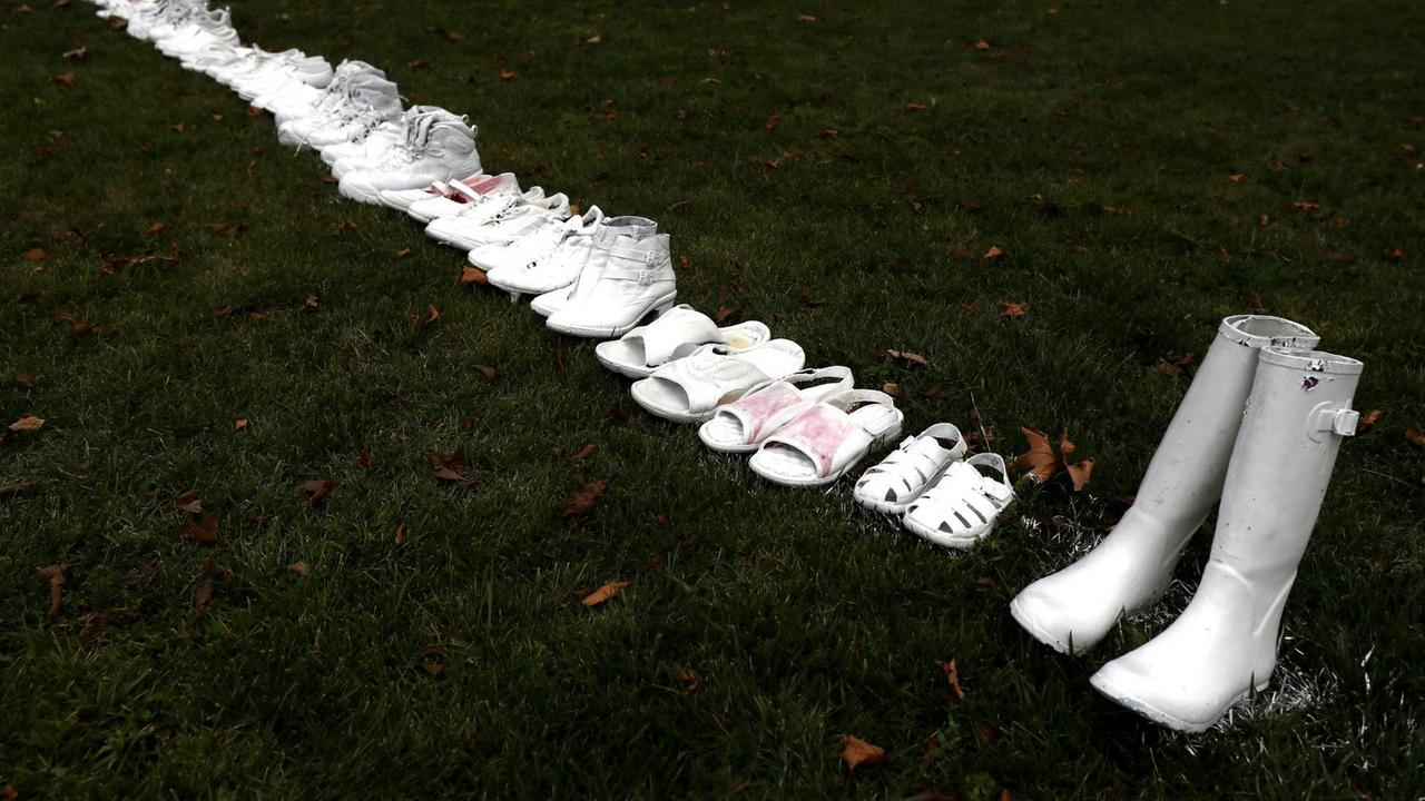 Eine Reihe weiß angesprühter Paar Schuhe zieht sich von oben links nach unten rechts durch das Bild. Eine Reihe weiß angesprühter Paar Schuhe zieht sich von oben links nach unten rechts durch das Bild.