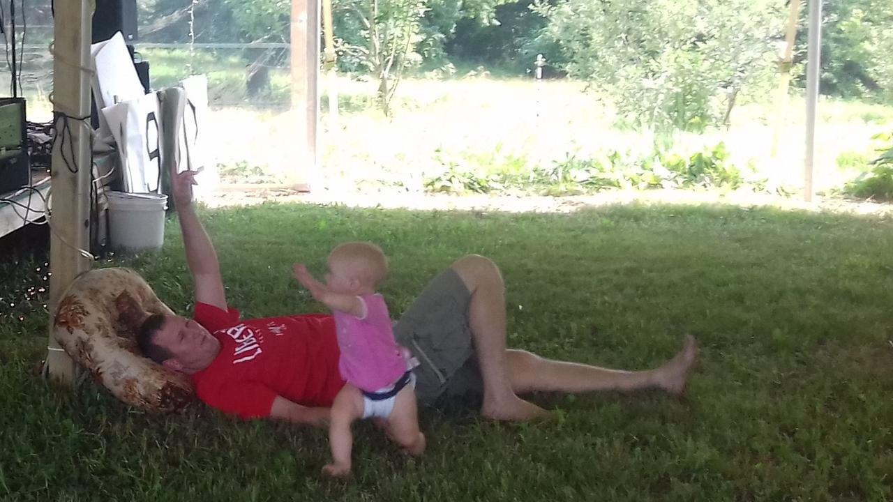Mann liegt auf der Wiese und Kind rennt um ihn herum