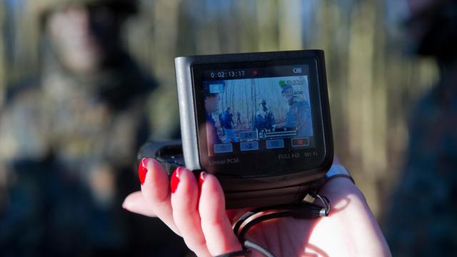 Eine weibliche Hand hält eine Kamera, mit der Soldaten gefilmt werden